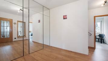 Een kamer met houten vloer, een grote spiegel en een deur naar een andere kamer.