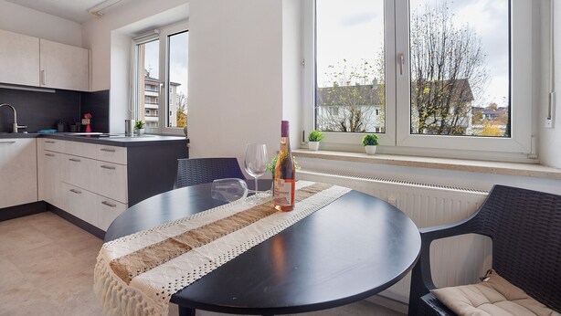 A modern kitchen with a dining area, a large window with a view, and a bottle of wine on the table. - Apartment 'Allgäu Space' with Shared Garden, Balcony and Wi-Fi (Marktoberdorf)