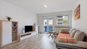 A modern living room with a sofa, TV, wooden shelving, and a dining area. - Apartment 'Allgäu Space' with Shared Garden, Balcony and Wi-Fi (Marktoberdorf)