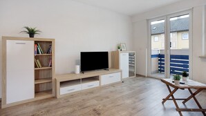 A room with a TV, wooden furniture, a bookshelf, and a sliding glass door to the outside. - Apartment 'Allgäu Space' with Shared Garden, Balcony and Wi-Fi (Marktoberdorf)