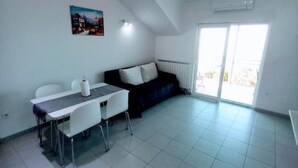A spacious living area with a dining table, chairs, a black sofa, and a large window. - Berti Sun & Sea Apartments (Hvar)