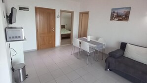 A modern living room with a dining area, a gray sofa, and a TV on a stand. - Berti Sun & Sea Apartments (Hvar)