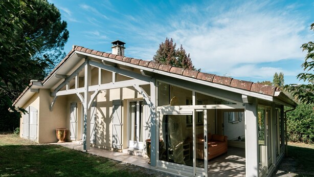 A house with a sloped roof, a covered porch, and a glass door leading to an interior space with a sofa. - LE COTTAGE - Charming 3 double bedroom villa - 10 minutes from the ocean (Saint-Julien-en-Born)