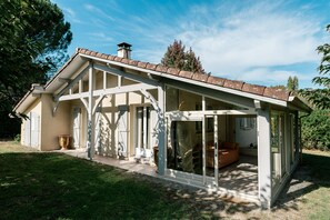 Une maison avec un toit en pente, une véranda et une porte vitrée donnant sur un espace intérieur où se trouve un canapé.