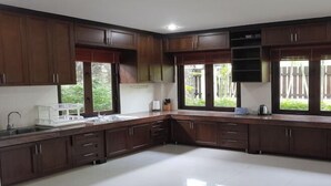 A kitchen with dark wooden cabinets, a white countertop, a sink, and a window with a view of greenery. - ViewPoint Villa (Phuket)