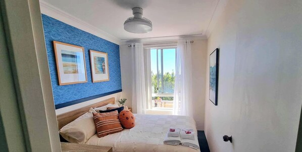 A bedroom with a bed, pillows, a ceiling fan, framed pictures, and a view of the outdoors. - The best climate in New South Wales, and arguably the best view in Flynns Beach! (Port Macquarie)