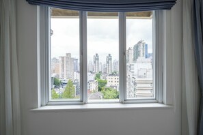 A window with a view of a cityscape, including high-rise buildings and greenery.