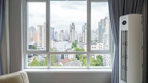 Ett rum med ett stort fönster som vetter mot staden, en vit luftkonditioneringsenhet och en beige soffa.