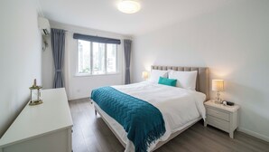 Ett hotellrum med en säng, sängbord, ett litet bord, ett fönster med gardiner och en taklampa.
