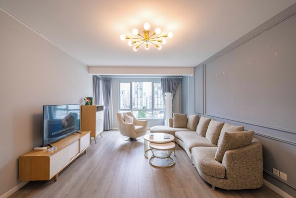 A modern living room with a flat-screen TV, a sofa, a coffee table, and a unique ceiling light fixture.