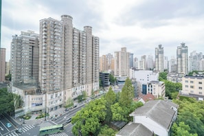 A high-rise residential building with multiple balconies, a street with vehicles, and surrounding greenery.