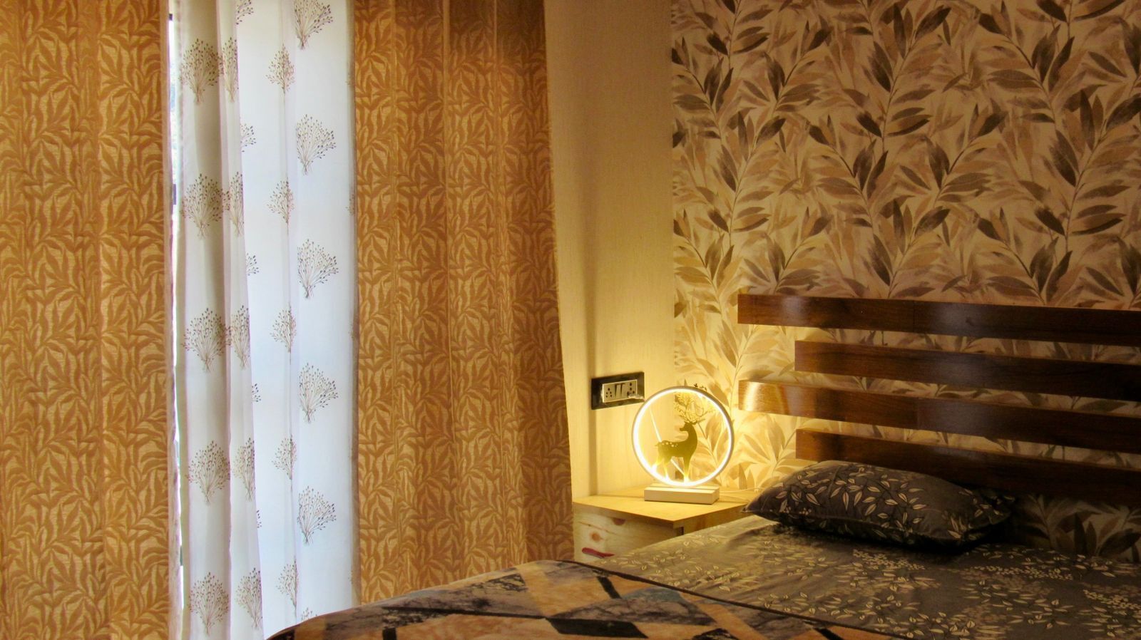 Et soveværelse med en seng, et sengebord med en lampe og væg med tapet med blad motiv.
