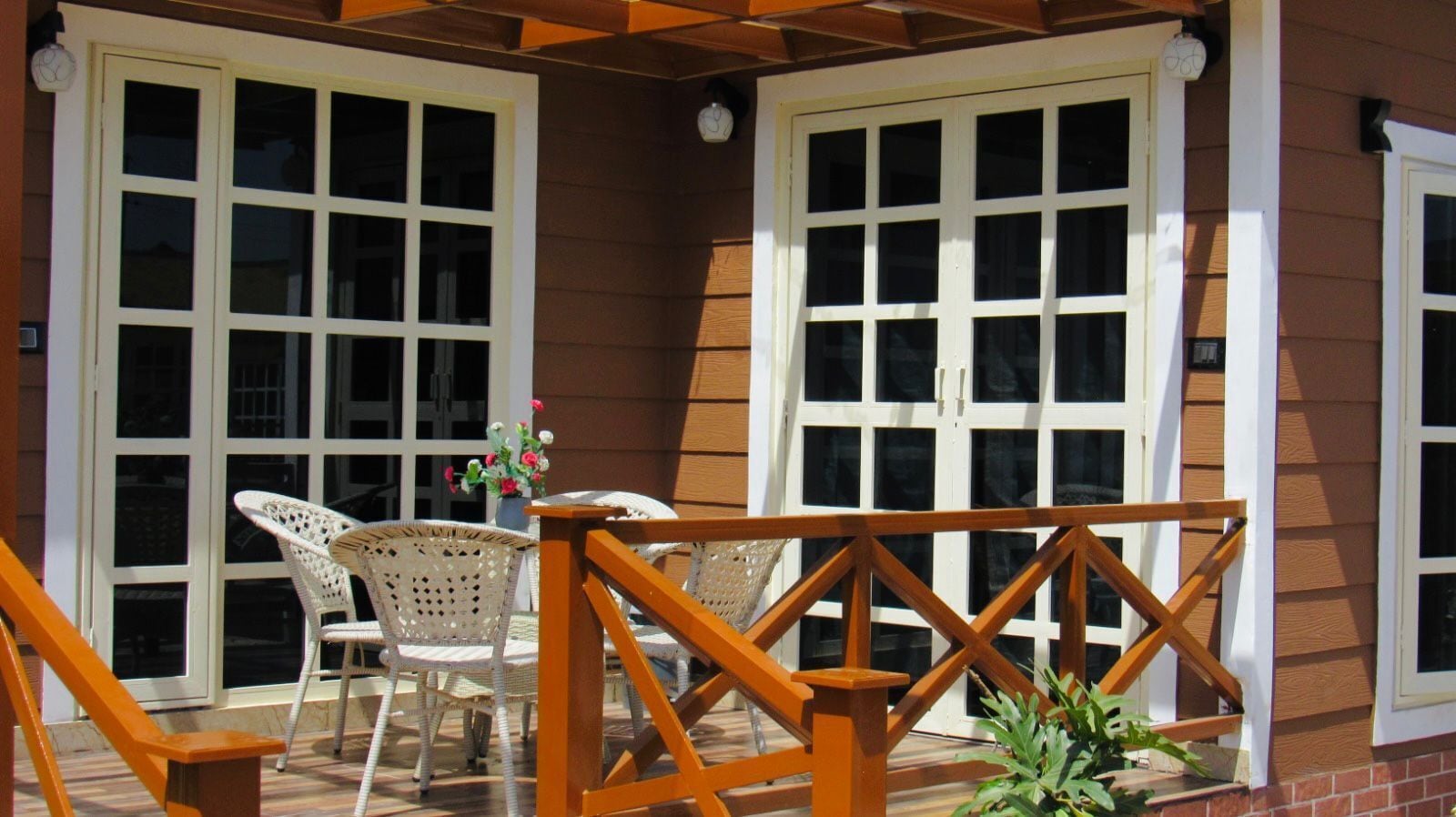 A covered patio with two white-framed windows, wicker chairs, and a wooden railing.