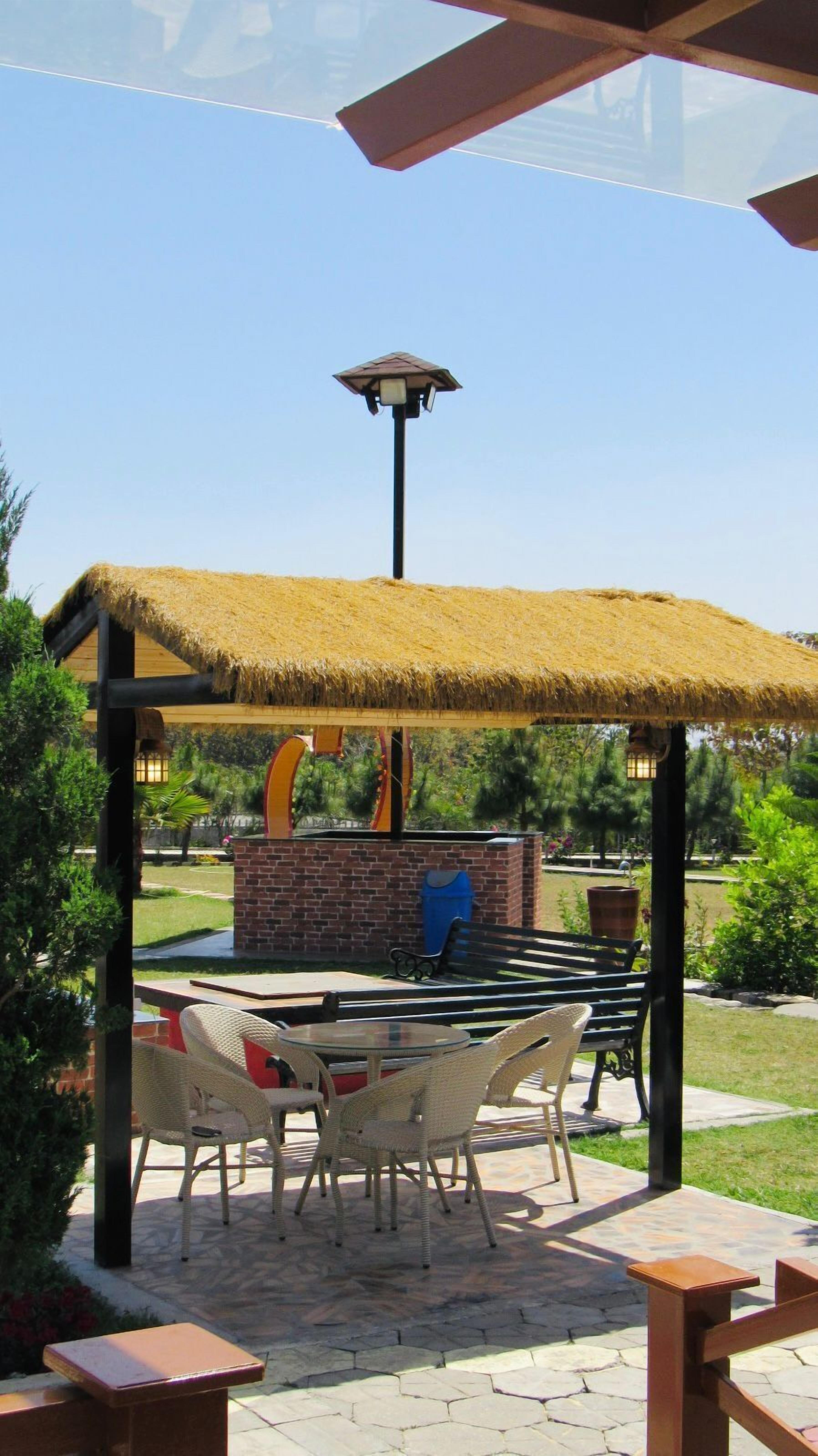 An outdoor patio area with a thatched roof gazebo, wicker furniture, and a brick fireplace.