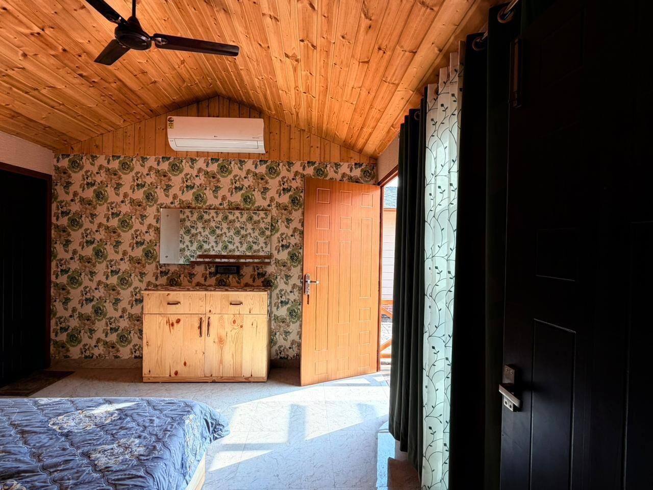 A bedroom with a wooden ceiling, a bed, a wooden dresser, a mirror, and a door.
