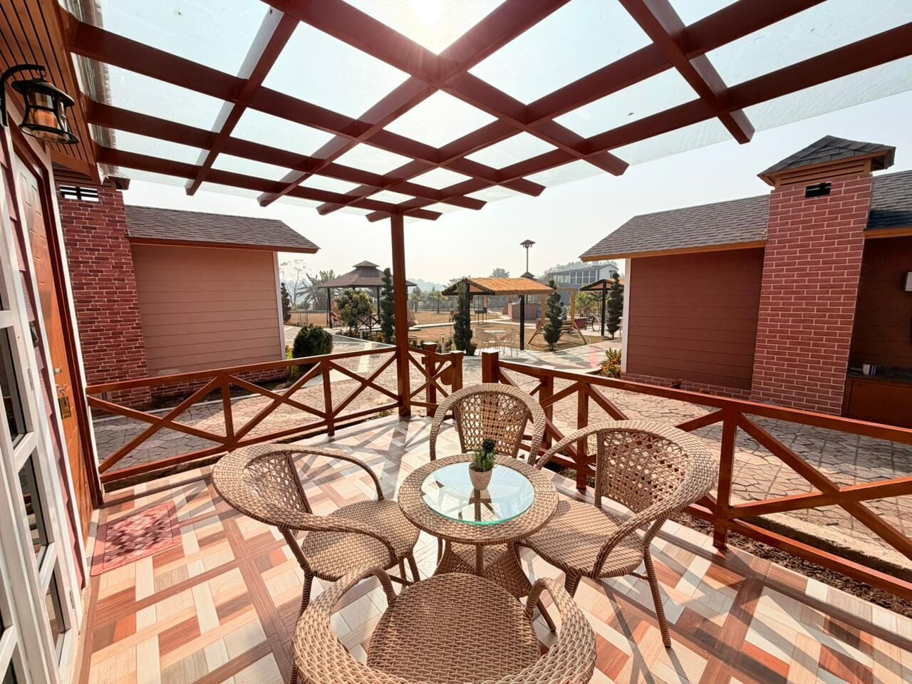 An outdoor patio with wicker furniture and a glass table, surrounded by a wooden pergola.