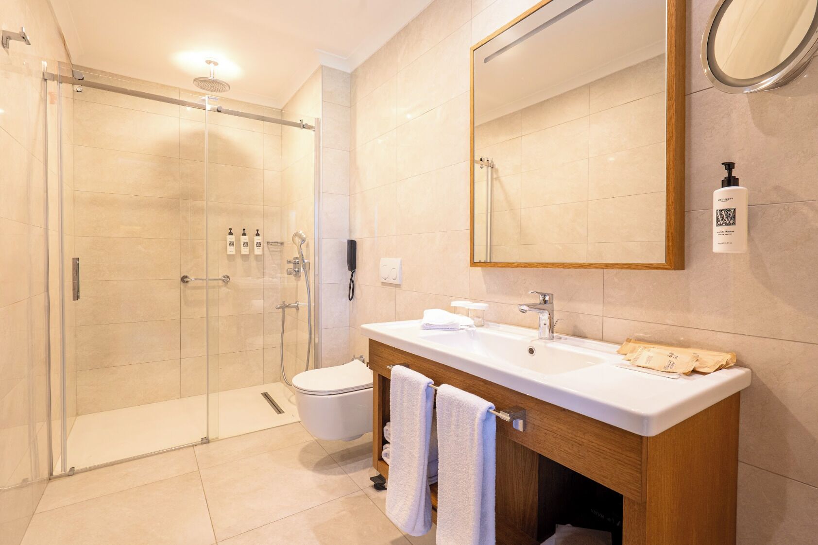 Un baño moderno con ducha envuelta en vidrio, un lavabo blanco y un espejo grande.