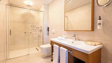 Un baño moderno con ducha envuelta en vidrio, un lavabo blanco y un espejo grande.