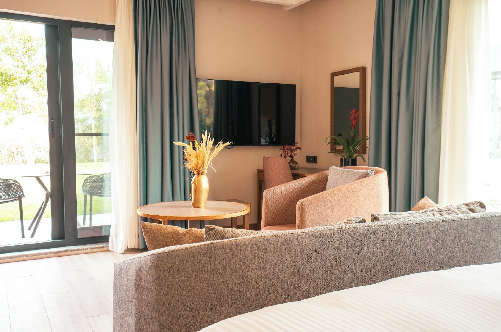 A hotel room with a bed, a sofa, a chair, a small table, and a TV.