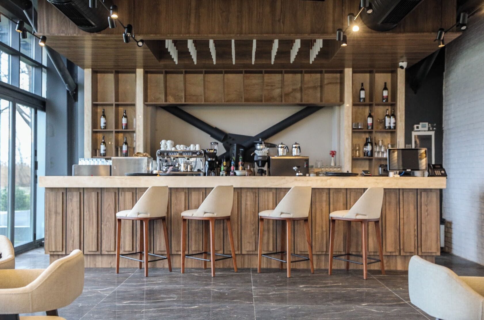 Una zona de bar con mostrador de madera, taburetes y una cafetera.