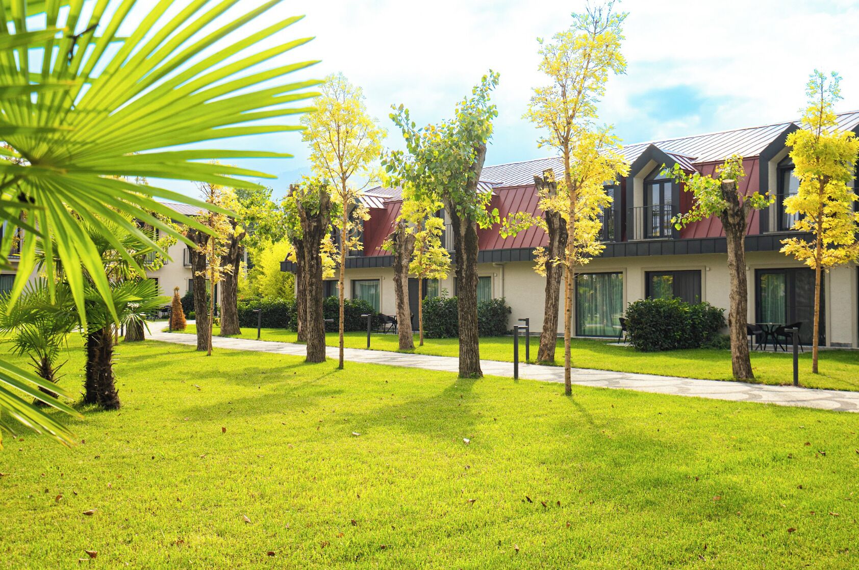A hotel with a modern design, featuring a well-maintained lawn, multiple trees, and a pathway leading to the building.