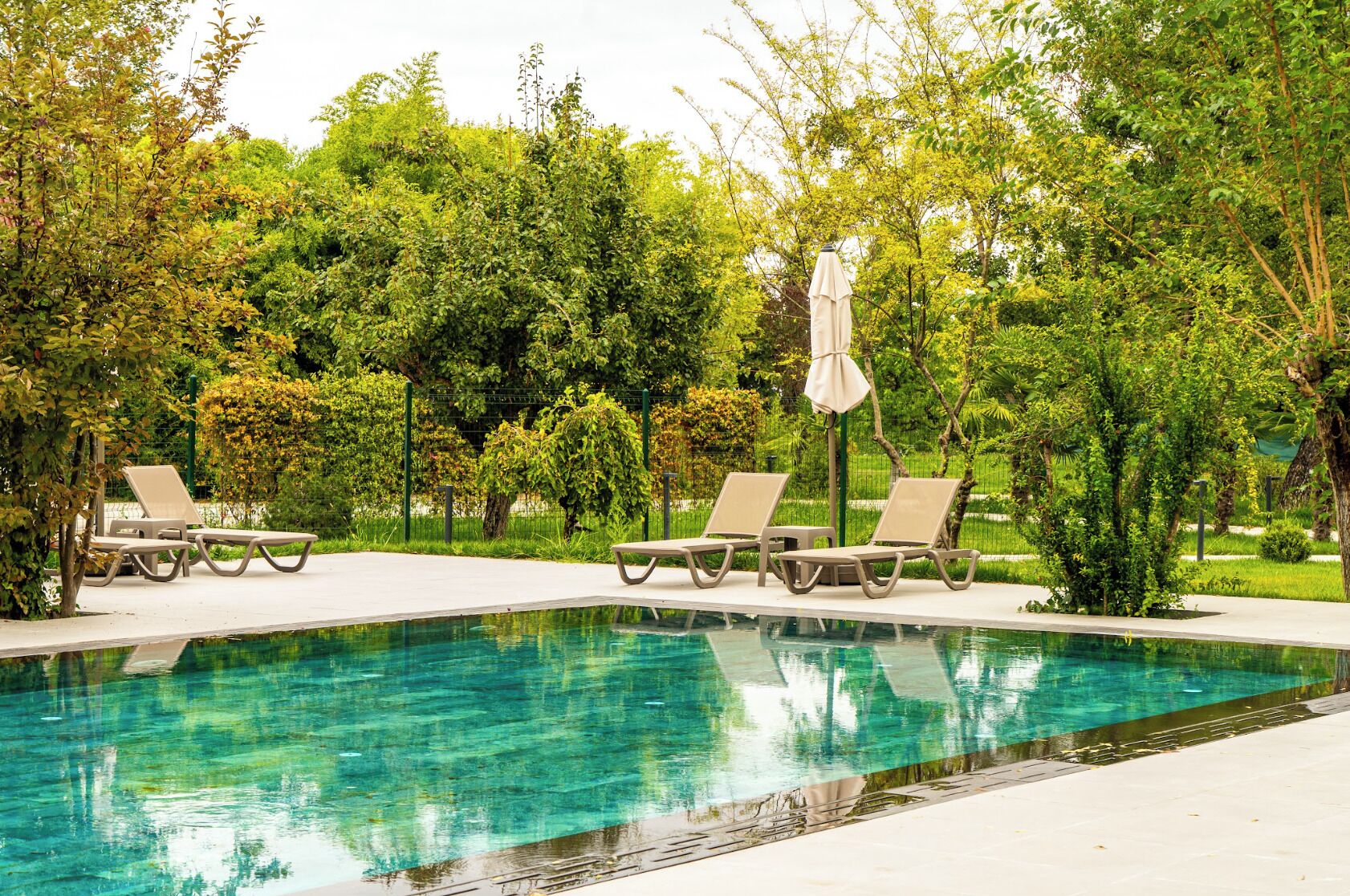A swimming pool with lounge chairs and an umbrella, surrounded by greenery.