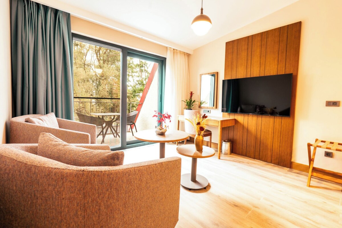 Un salon avec un canapé, une table ronde, un téléviseur et un balcon équipé d’une chaise.