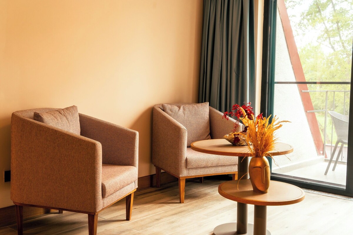Een kamer met twee fauteuils, een klein rond tafeltje en een vaas met gedroogde bloemen.