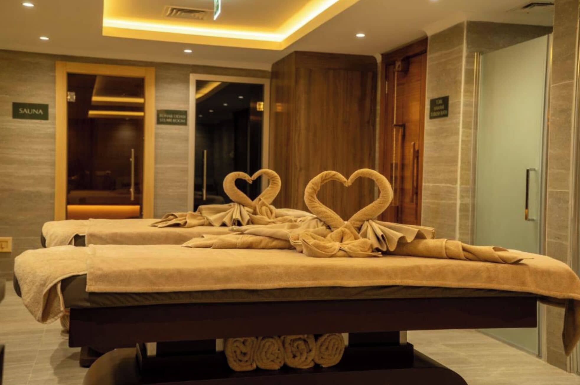 Une chambre d’hôtel avec deux lits, un panneau indiquant la présence d’un sauna et une décoration en forme de cœur faite avec une serviette.