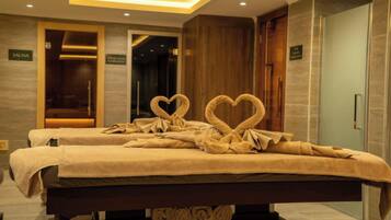 Une chambre d’hôtel avec deux lits, un panneau indiquant la présence d’un sauna et une décoration en forme de cœur faite avec une serviette.