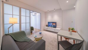 Una sala de estar moderna con un sofá, una mesa de centro, un televisor y una zona de comedor con una mesa y sillas.
