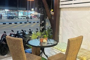 Un coin salon avec des fauteuils en osier et une petite table, une plante en pot, et une vue sur la rue.