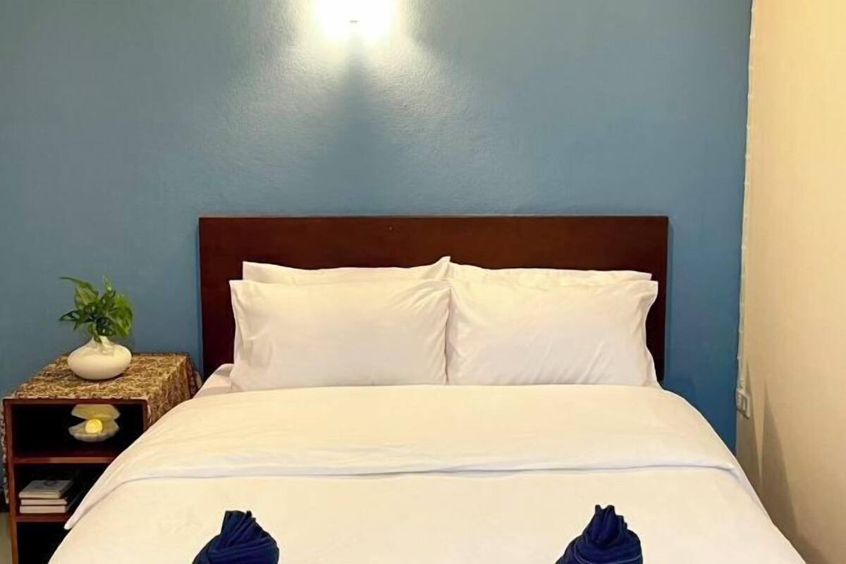 Un lit bien fait, avec du linge de lit blanc et deux serviettes bleues au pied du lit.