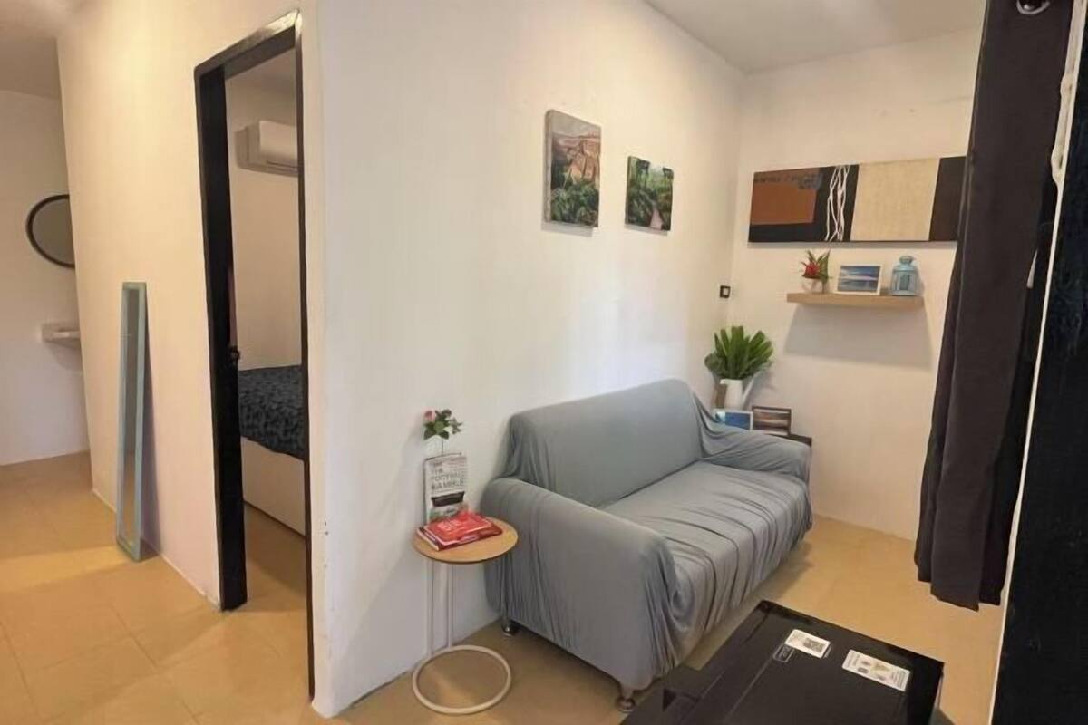 Un petit salon moderne avec un canapé gris, une petite table d’appoint sur laquelle se trouvent un livre et une plante, et une étagère murale agrémentée d’objets décoratifs.