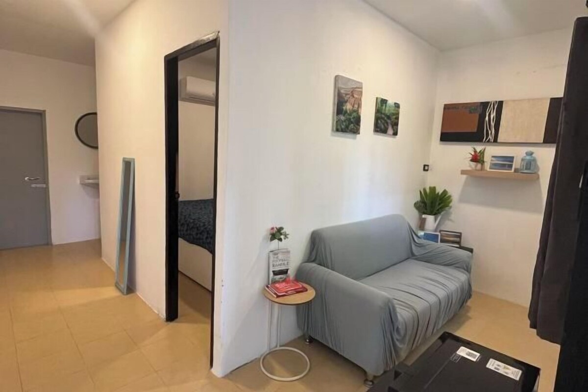 Een moderne woonkamer met een grijze bank, een klein rond tafeltje met een boek en een kamerplant.
