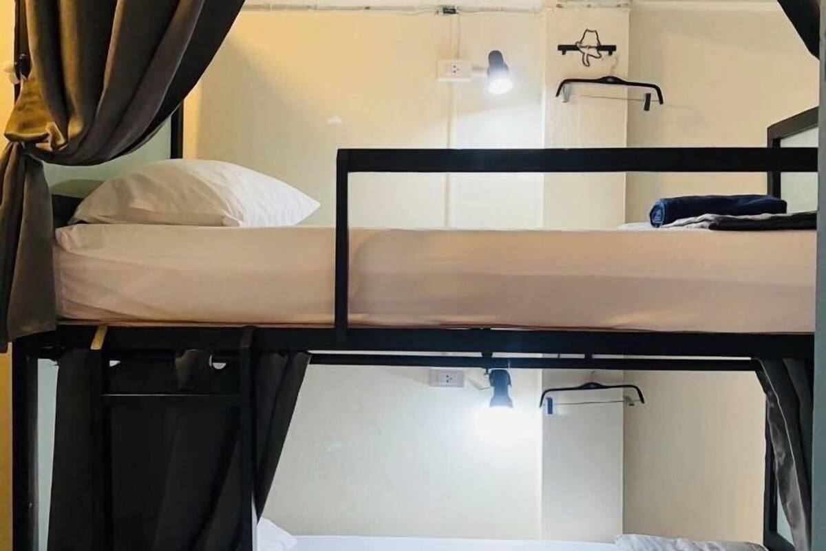 Une chambre avec un lit superposé, une tête de lit, un luminaire suspendu et une prise électrique fixée au mur.
