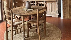 Un comedor rústico con una mesa y sillas de madera, una lámpara colgante de fibras, un espejo y jarrones decorativos sobre un aparador de madera.