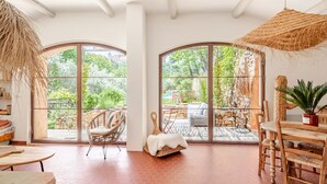 Amplia habitación con grandes ventanales de arco, una silla de mimbre, una mesa de comedor de madera y un sillón colgante de ratán.