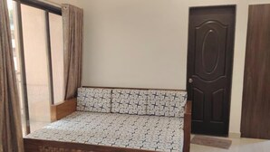 A room with a patterned sofa, a dark wooden door, and a window with curtains. - Mudra Villa & Resort (Nagaon)