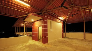 A covered outdoor area with a red brick wall, a door, and a small window. - Mudra Villa & Resort (Nagaon)