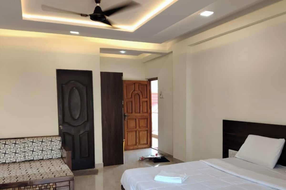 A hotel room with a bed, a sofa, a ceiling fan, and a wooden door.