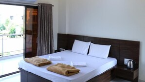 A modern hotel room with a large bed, a ceiling fan, and a view of the outdoors. - Mudra Villa & Resort (Nagaon)