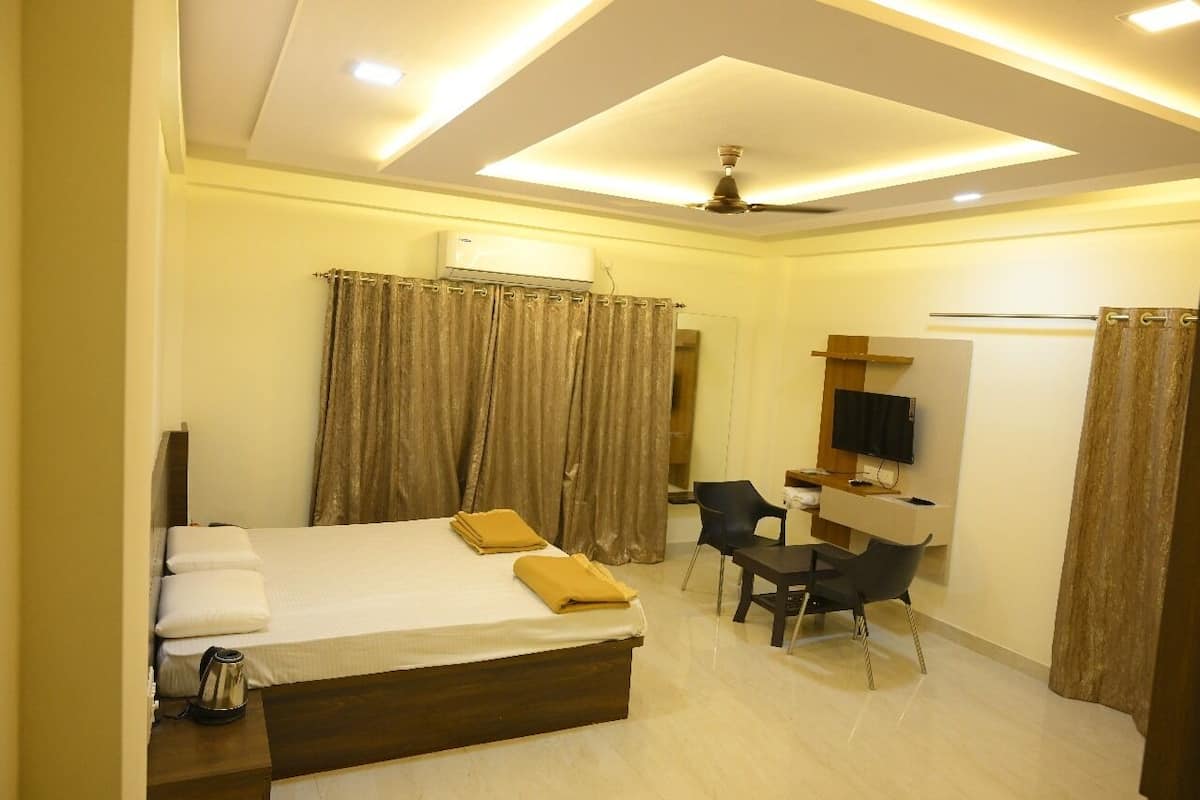 A hotel room with a bed, a desk, a chair, a television, and an air conditioning unit.