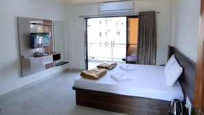 A hotel room with a bed, a TV, a ceiling fan, an air conditioner, and a view of the outside. - Mudra Villa & Resort (Nagaon)
