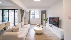 Een moderne woonkamer met een grote bank, een ronde salontafel, een flatscreen televisie en een eethoek met stoelen en een tafel.