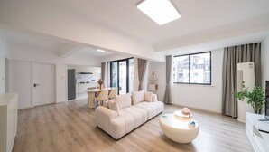 Een moderne woonkamer met een beige bank, een ronde salontafel, en een eethoek met een tafel en stoelen.
