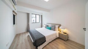 Een moderne slaapkamer met een bed, nachtkastje, lamp en een raam met gordijnen.