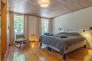 Een slaapkamer met een houten plafond, een bed met een geruit sprei, een stoel en een raam met gordijnen.