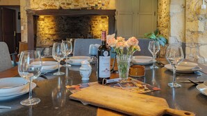 Une table à manger dressée avec des verres à vin, des assiettes et une bouteille de vin, le tout sur fond d’un mur en pierre et d’une cheminée.