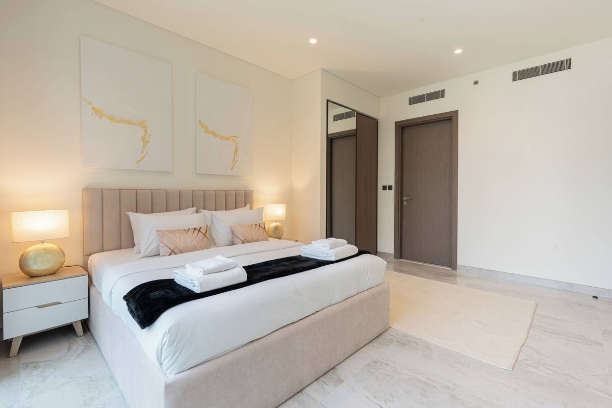 A modern bedroom with a large bed, bedside lamps, and artwork on the wall.